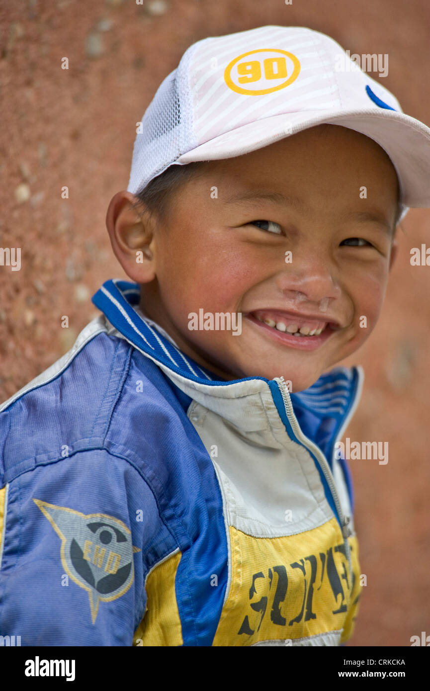 A cheeky smiling young Tibetan Chinese boy with mucus dribbling from his nose poses for the camera. Stock Photo