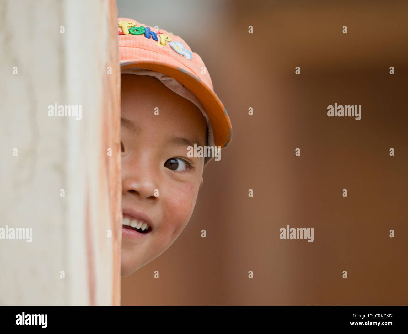 A young Tibetan Chinese boy playing peek-a-boo around a corner at the camera. Stock Photo