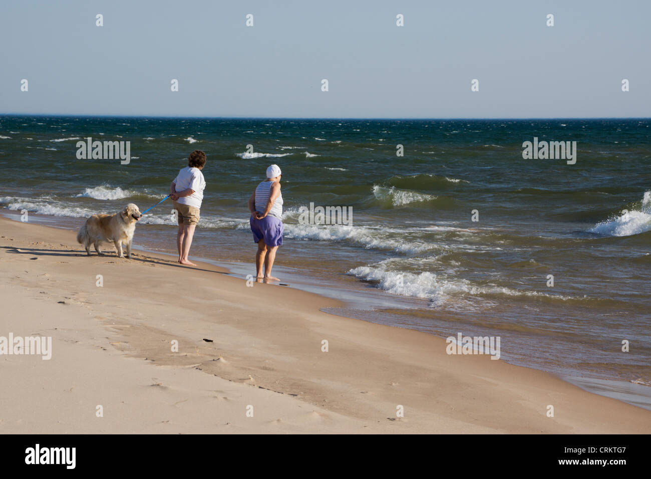 Two elderly women and their dog watch waves roll in from Lake Michigan. Stock Photo