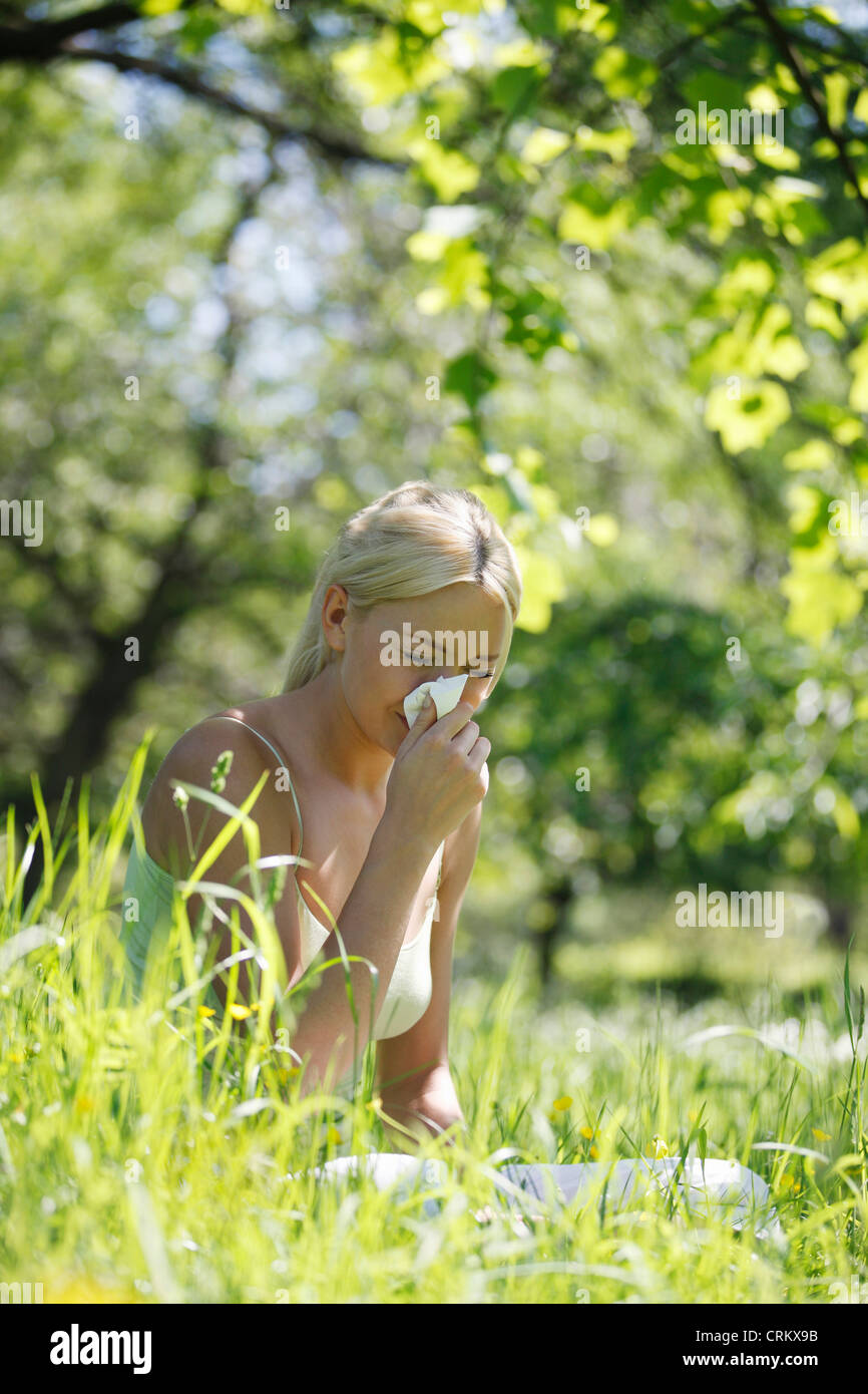 A young blond woman sneezing into a tissue Stock Photo