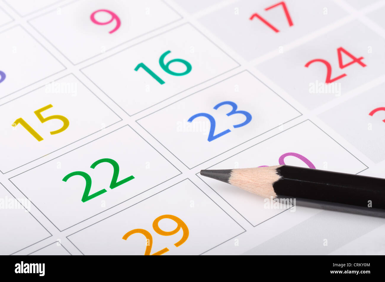 Black pencil on calendar page with colorful dates Stock Photo