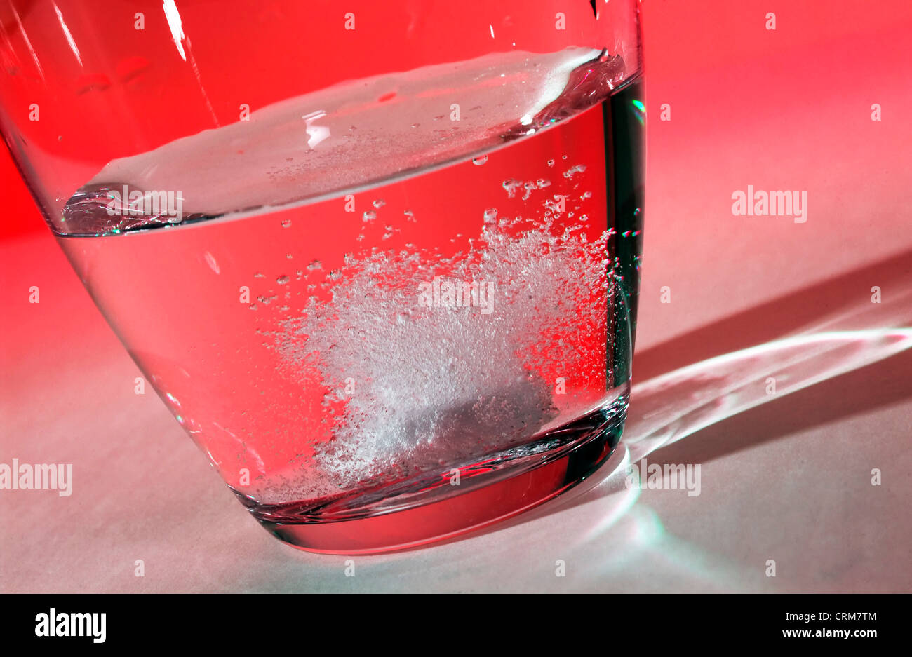 Tablet effervescing as it dissolves in a glass of water against a red background. Stock Photo