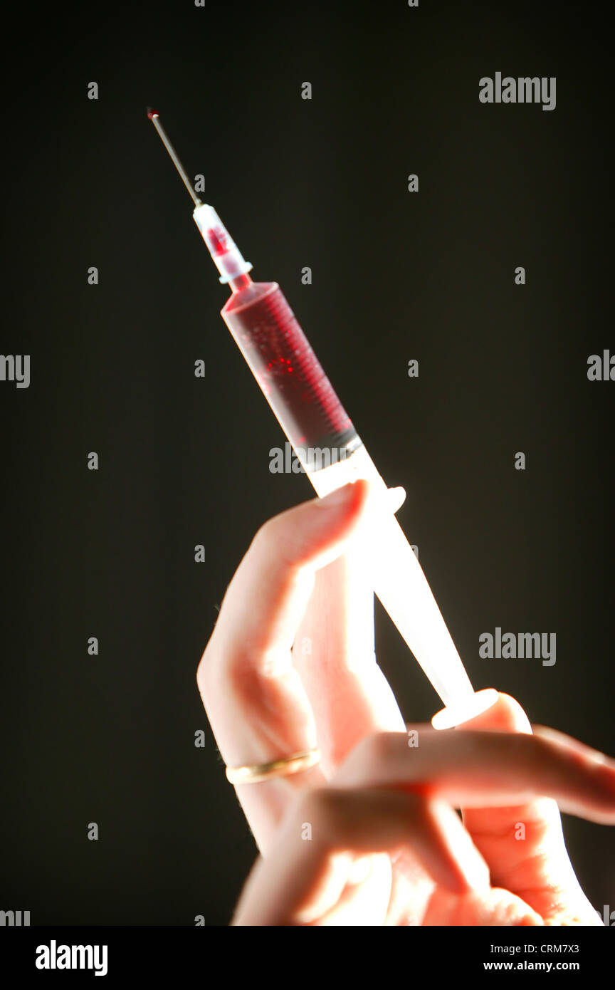 A disposable hypodermic syringe containing red fluid being held against a black background. Stock Photo
