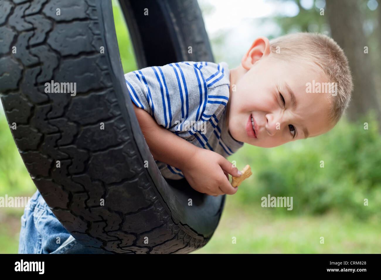 Portrait of a young boy winking while swinging on tire Stock Photo