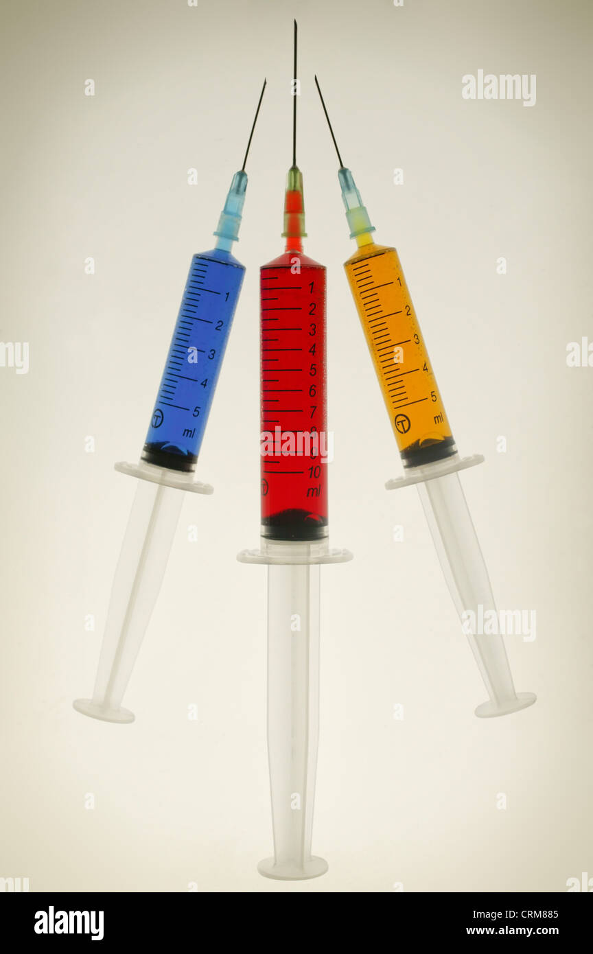 Three disposable hypodermic syringes containing blue, red and yellow