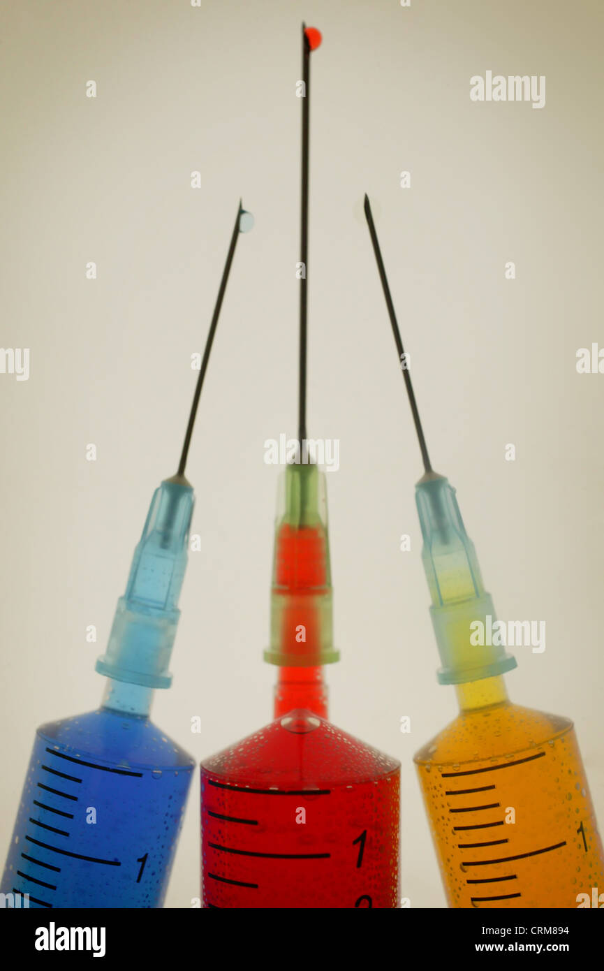 Three disposable hypodermic syringes containing different coloured