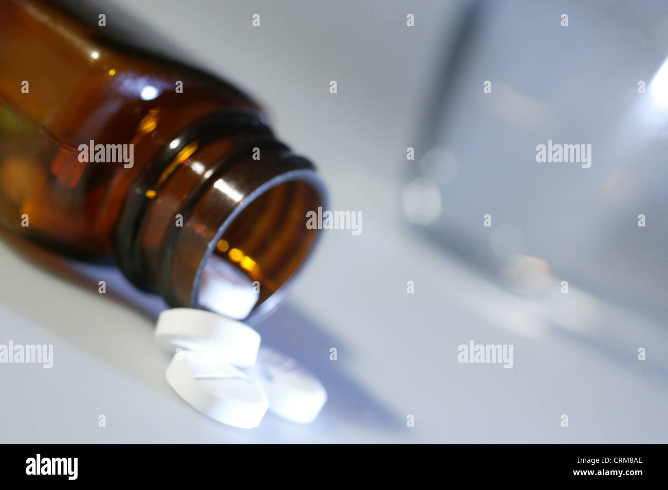White paracetemol tablets spilling out of a brown bottle near a glass of water. Stock Photo