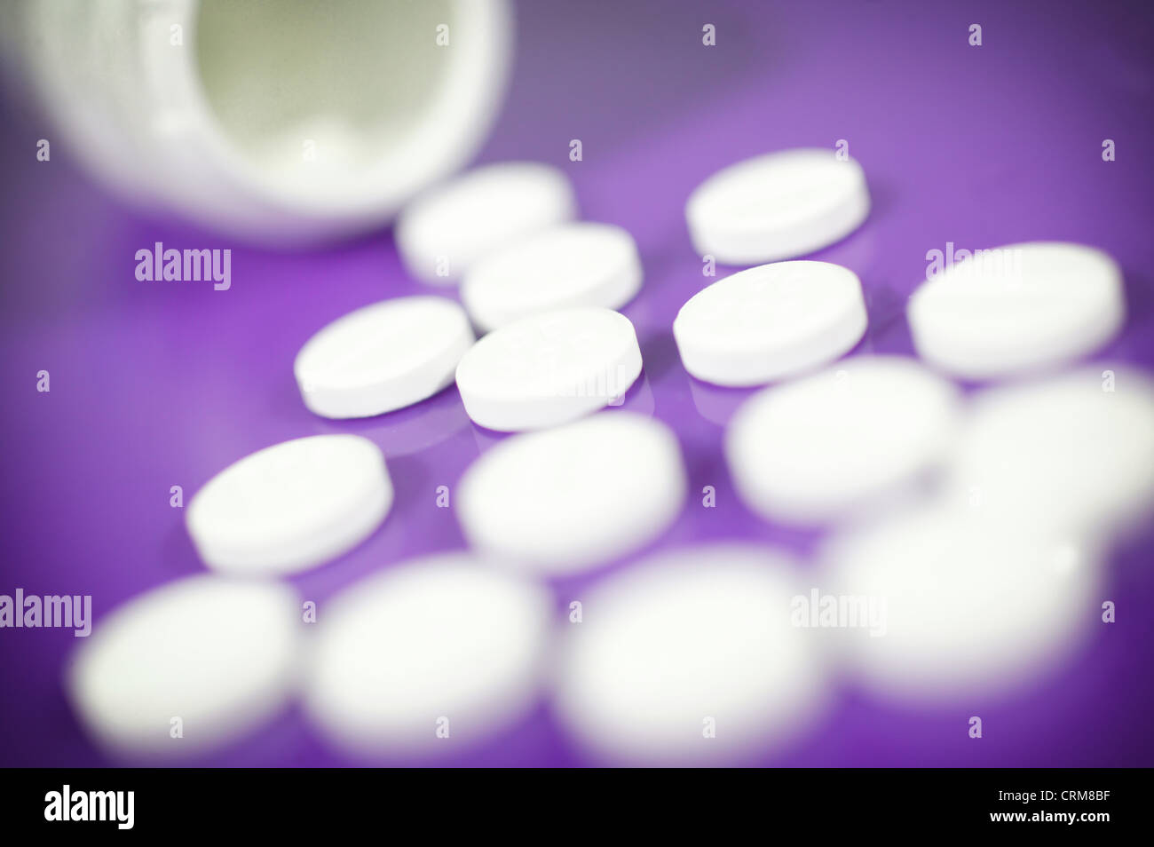 White paracetamol tablets spilling from a bottle against a purple background. Stock Photo