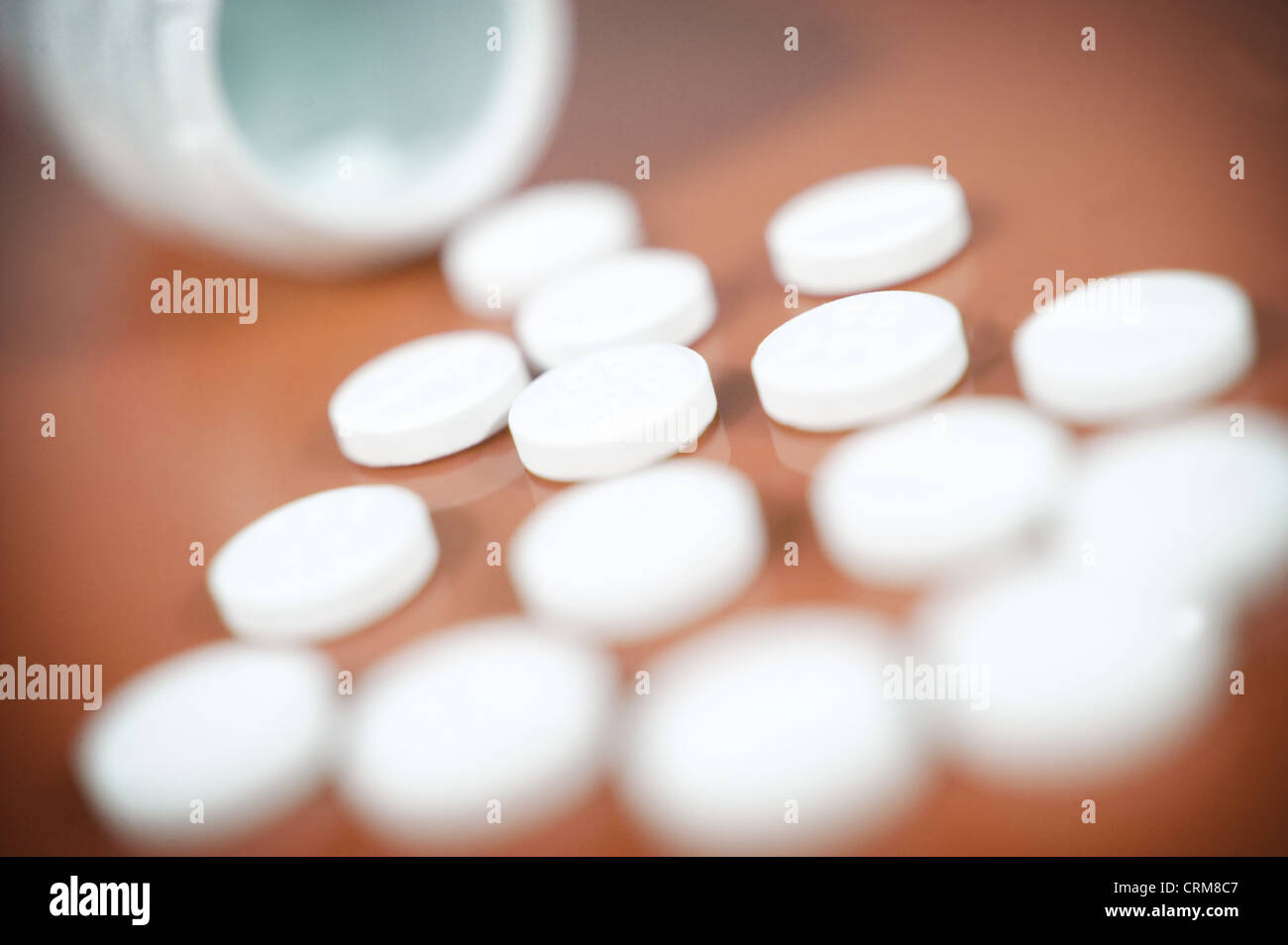 White paracetamol tablets spilling from a bottle against a brown background. Stock Photo