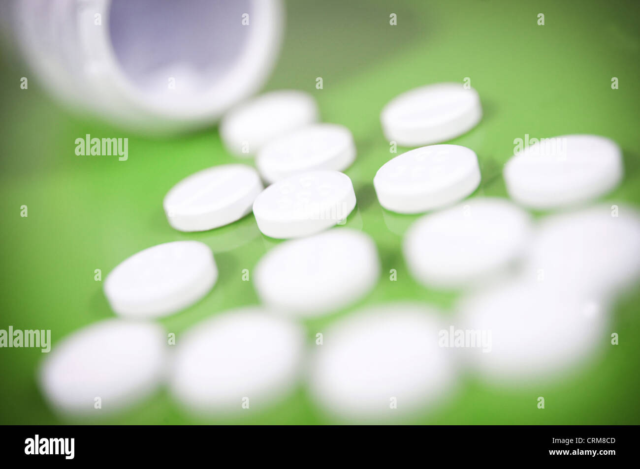 White paracetamol tablets spilling from a bottle against a green background. Stock Photo