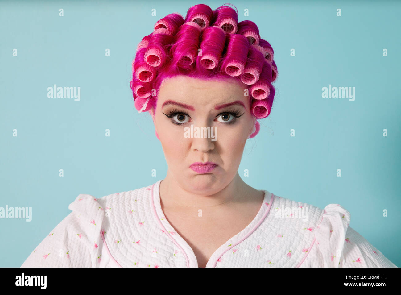 Portrait of young woman grimacing with hair curlers over colored background Stock Photo