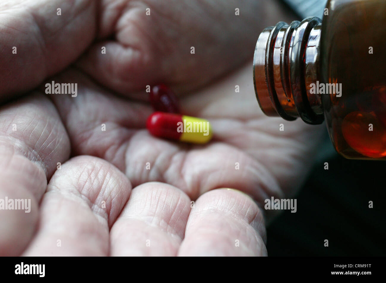 Hand of an elderly man pouring a small assortment of pills onto the palm of her hand. Stock Photo