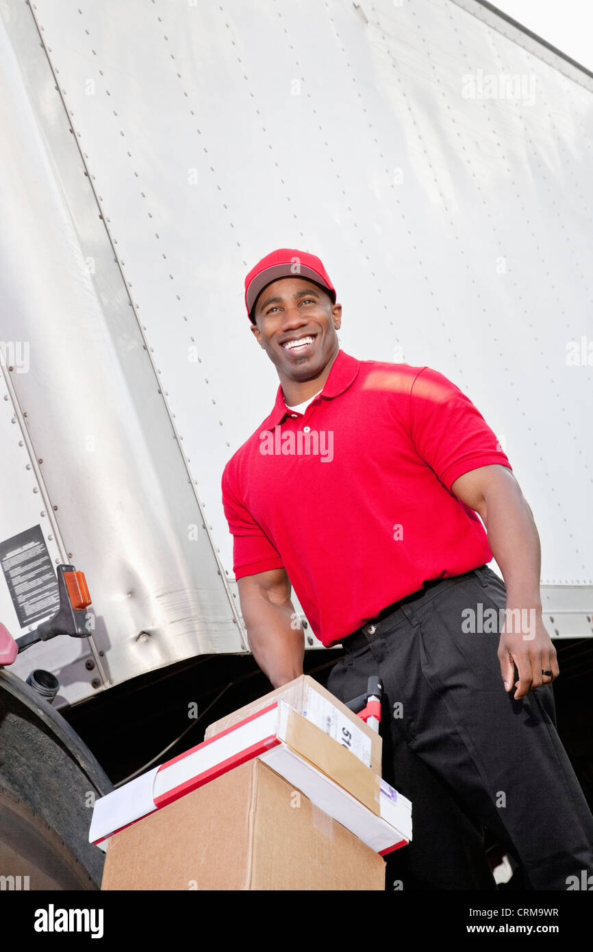Cheerful young delivery person pushing handtruck Stock Photo