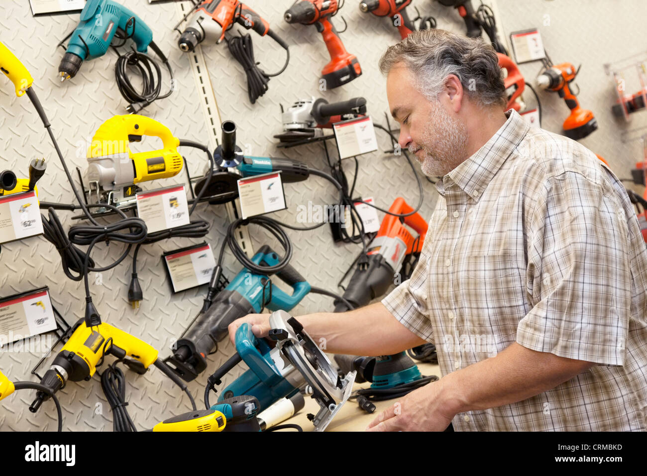 Side view of mature salesperson looking at electric saw Stock Photo