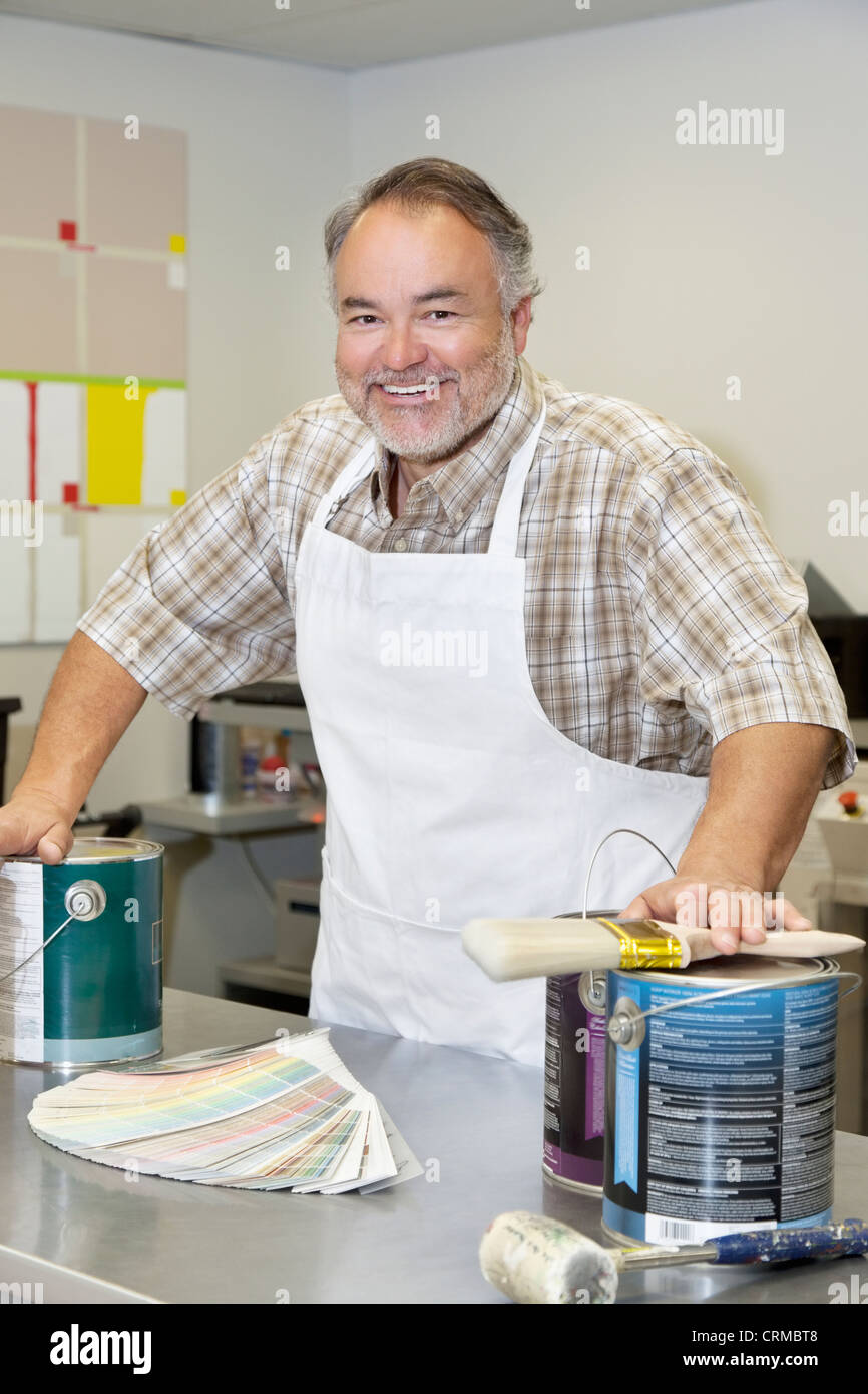 Portrait of a cheerful mature store clerk with paint cans and brush in