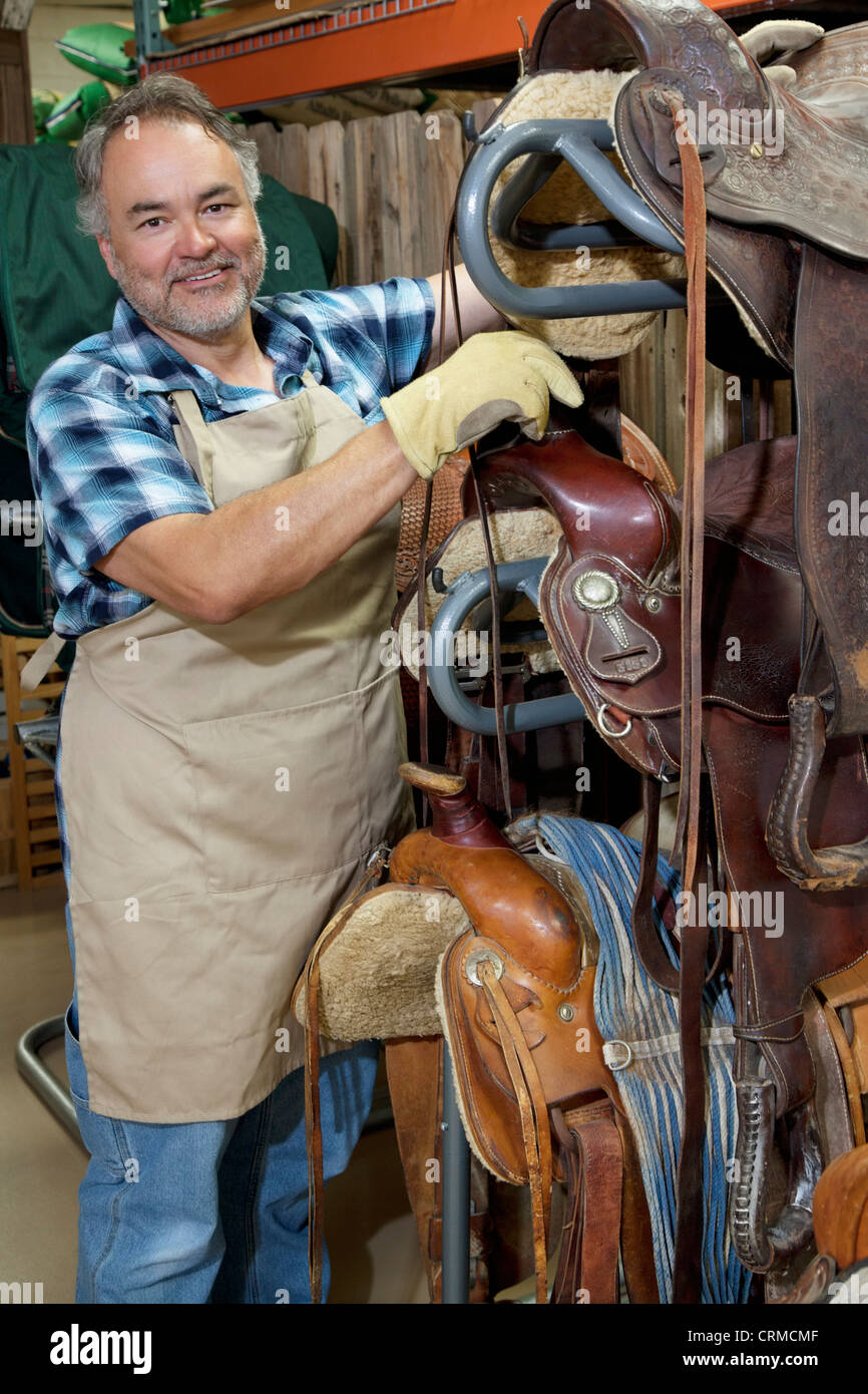 Portrait of a happy mature salesperson standing by horse riding tack in feed store Stock Photo