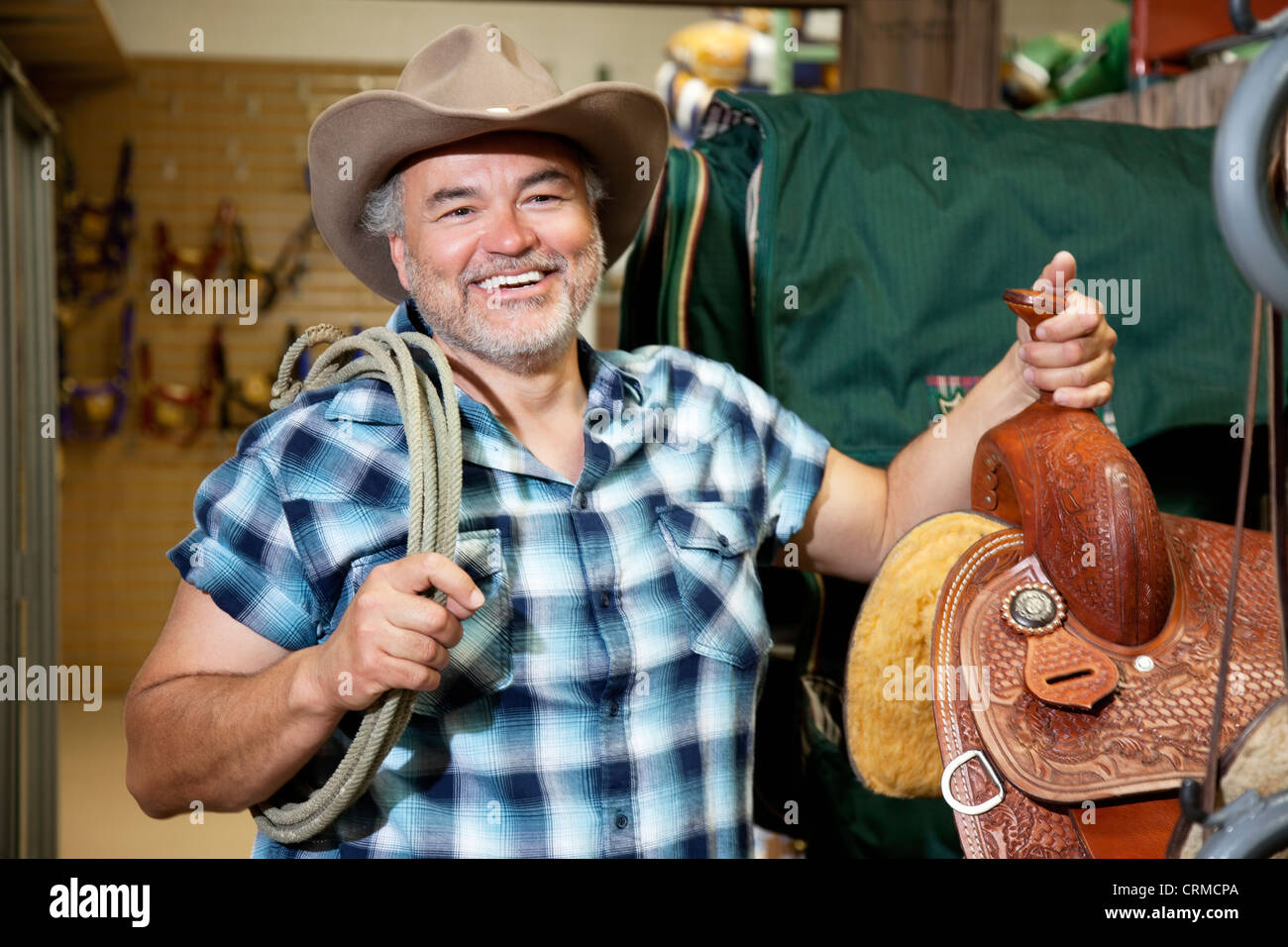 Happy mature cowboy with saddle and rope in feed store Stock Photo