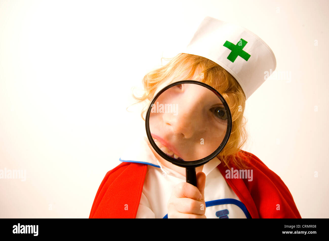 Young girl dressed as a nurse looks through a magnifying glass Stock