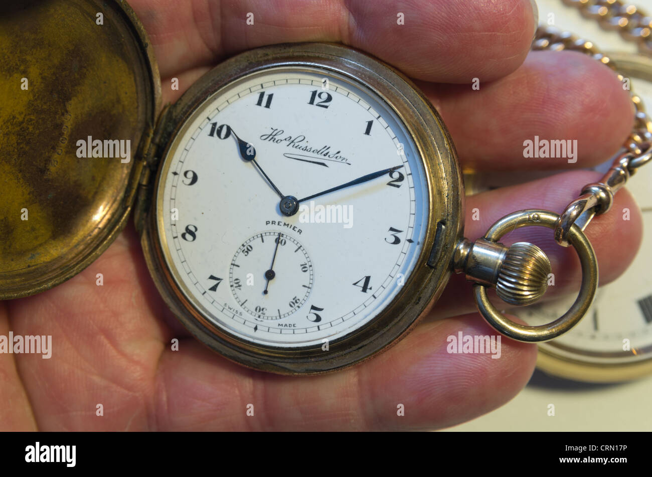 A tarnished gold pocket watch with front cover opened to show watch