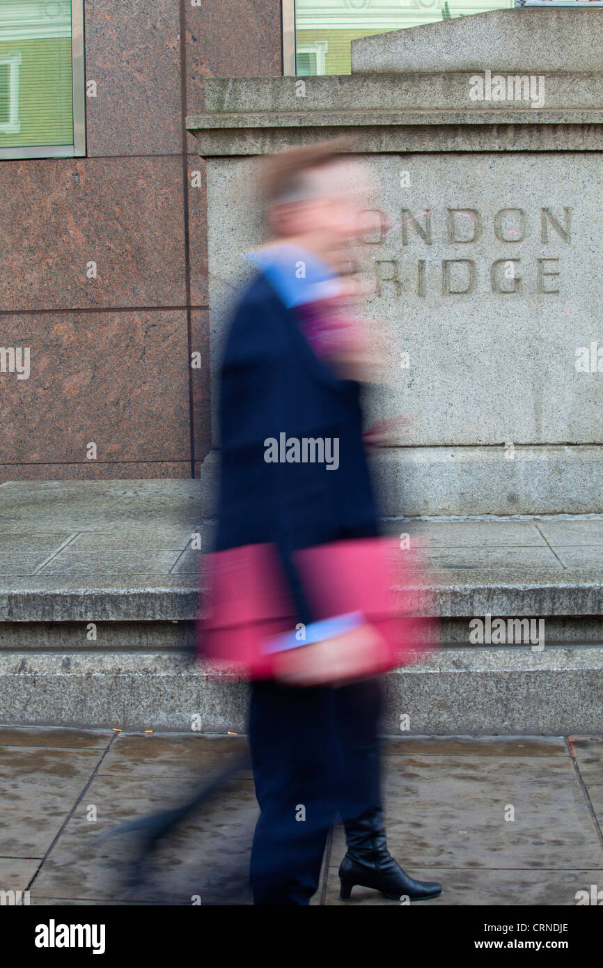 A man and woman walking past a stone plinth with London Bridge carved into it. Stock Photo
