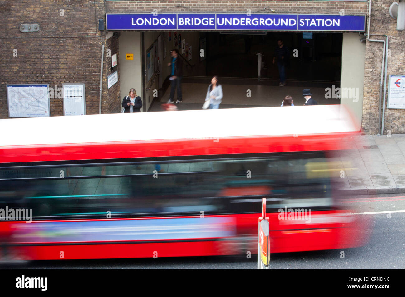 A red London bus passing an entrance to London Bridge Underground Station. Stock Photo