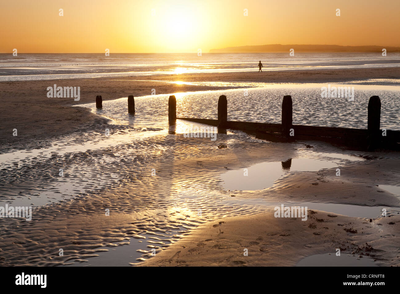 Silhouette of a lone person walking along the seashore at Camber Sands during sunset. Stock Photo