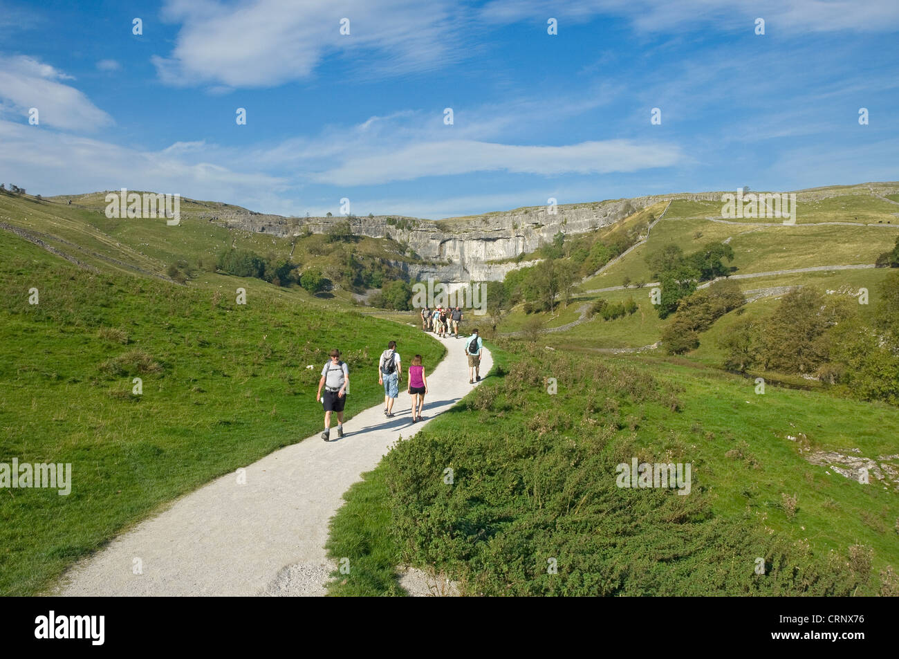 People walking along a footpath leading to Malham Cove, a spectacular curved limestone formation in the Yorkshire Dales National Stock Photo
