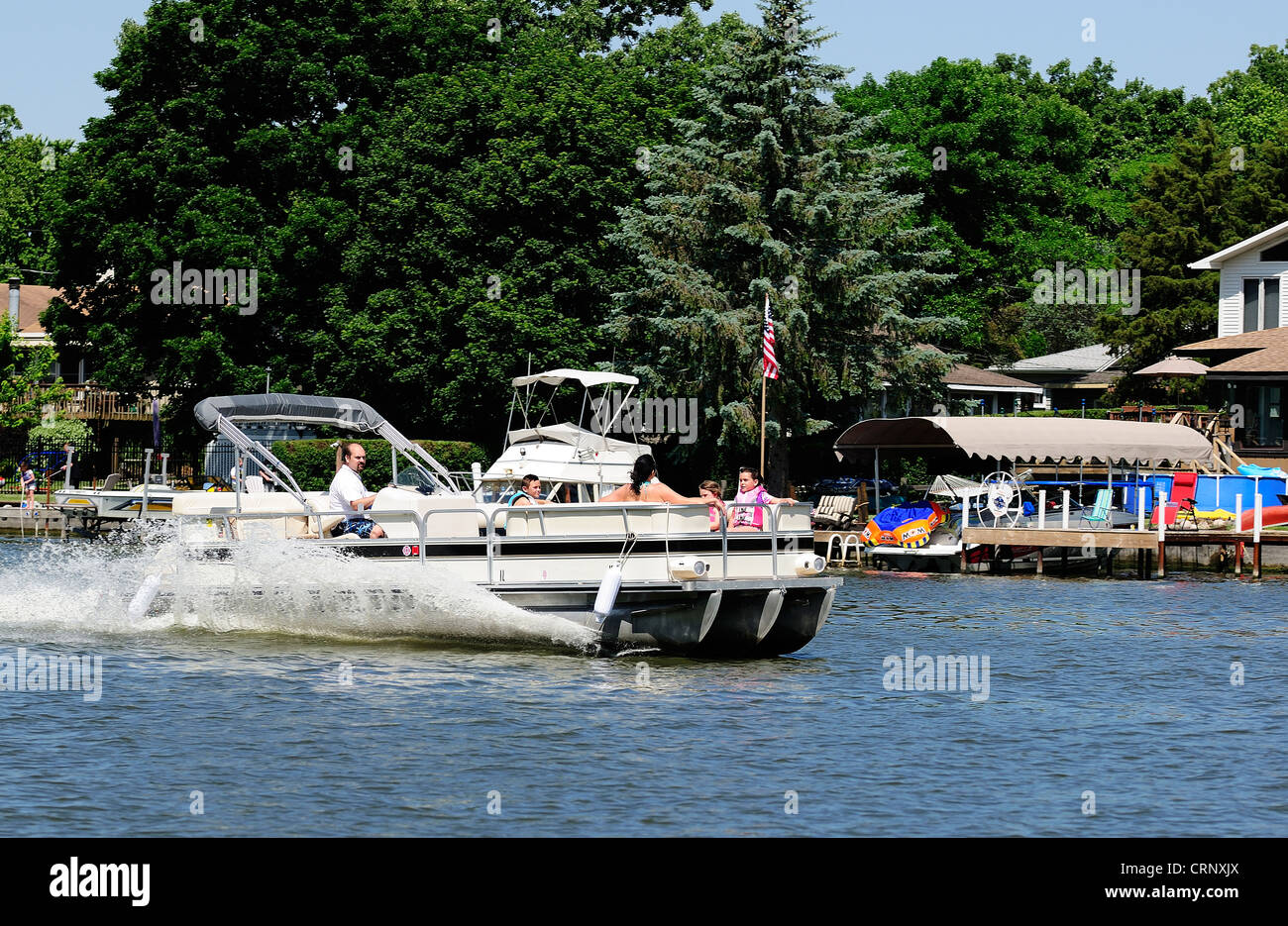 Pontoon boat with family aboard cruising along shoreline. Stock Photo