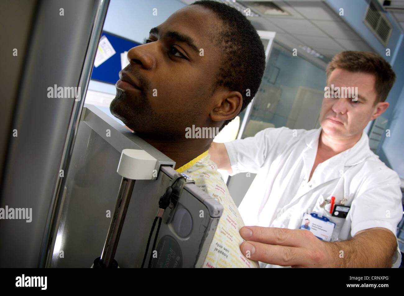 A radiologist x-rays a male patient who is standing in front of the x-ray machine. Stock Photo