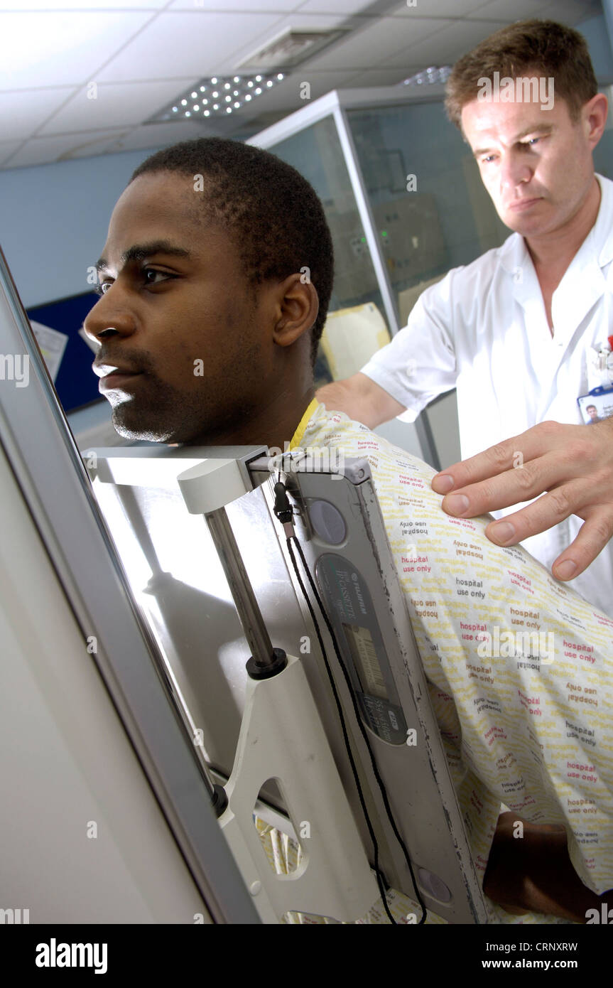 A radiologist x-rays a male patient who is standing in front of the x-ray machine. Stock Photo