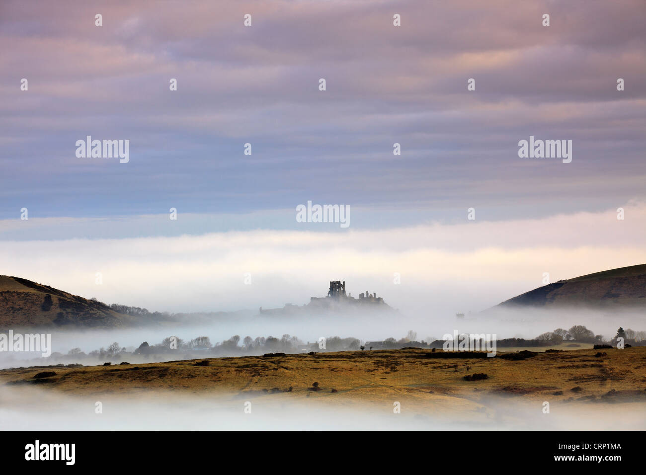 Mist around Corfe Castle viewed from Kingston, showing its position guarding the only gap in the Purbeck Hills for 12 miles. Stock Photo