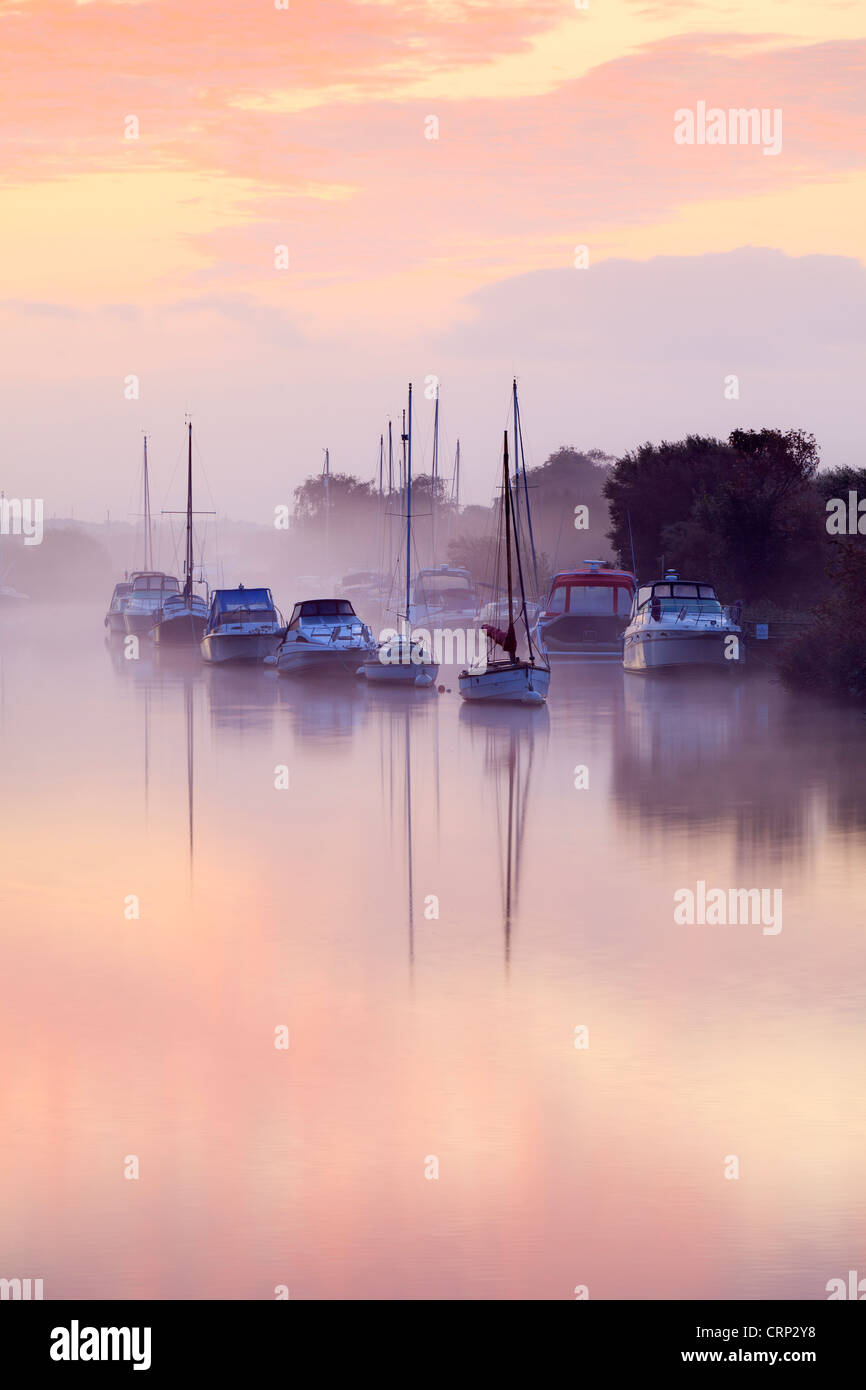 Early morning mist lingering over small pleasure boats moored on the River Frome at Wareham Quay. Stock Photo
