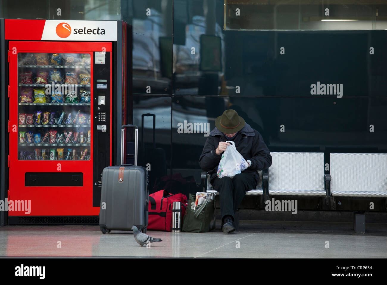 A passenger sitting with holdalls next to a vending machine on a platform at Newcastle Central Station. Stock Photo