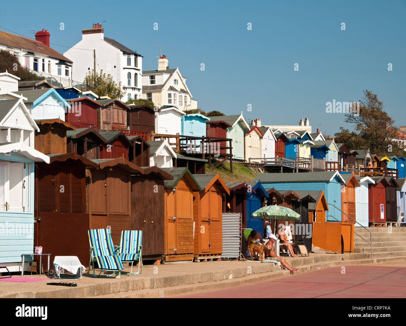 People relaxing in front of beach huts along the seafront at Walton-on-the-Naze. Stock Photo