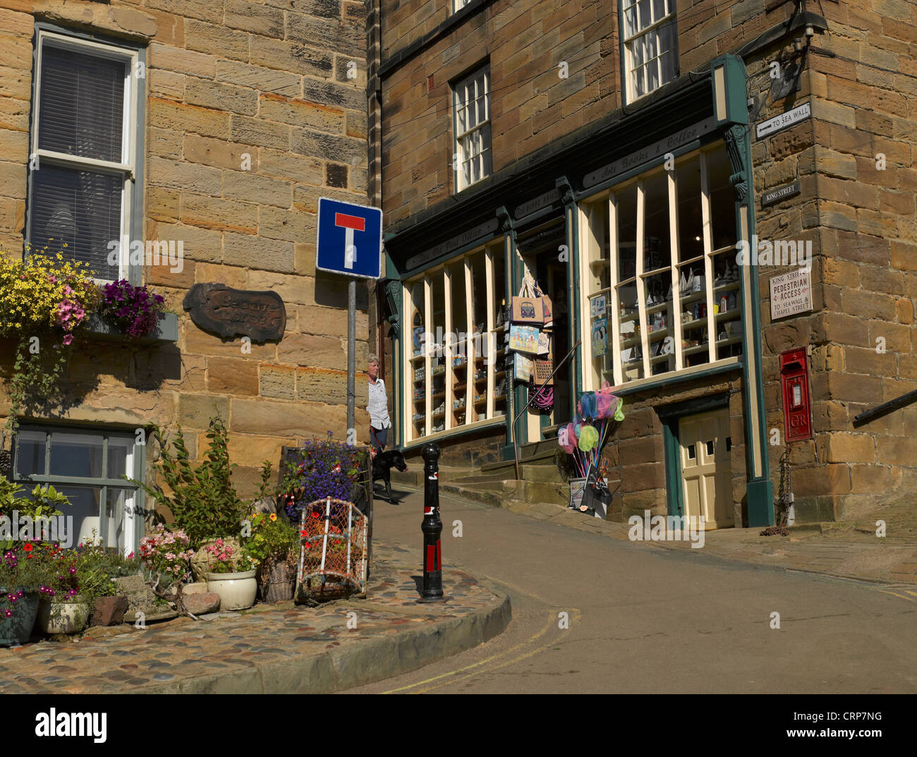 A woman walking her dog down King Street in the fishing village of Robin Hood's Bay, once the busiest smuggling community on the Stock Photo