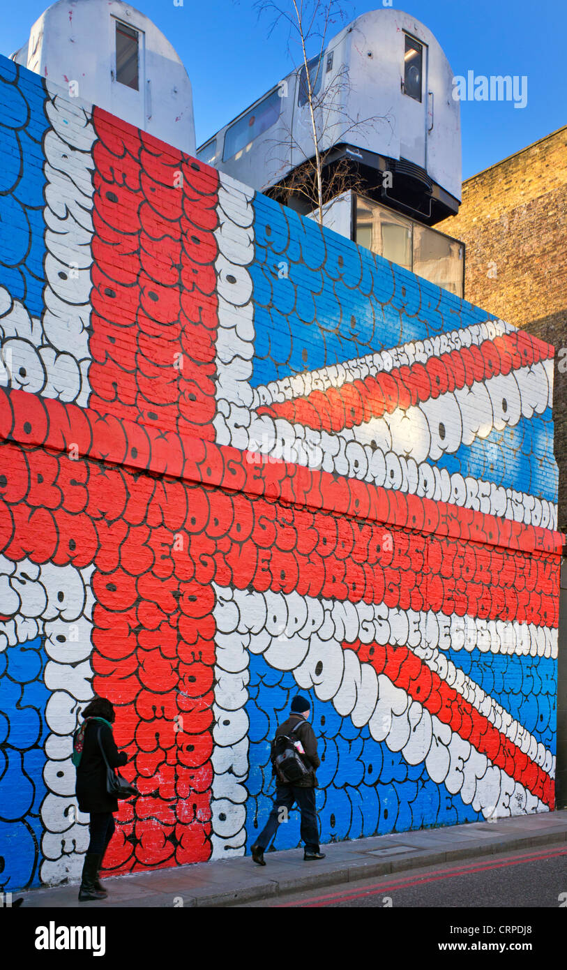 Londoners walk to work past an image of the Union flag painted on a wall in bubble letters in the East End of London. Stock Photo