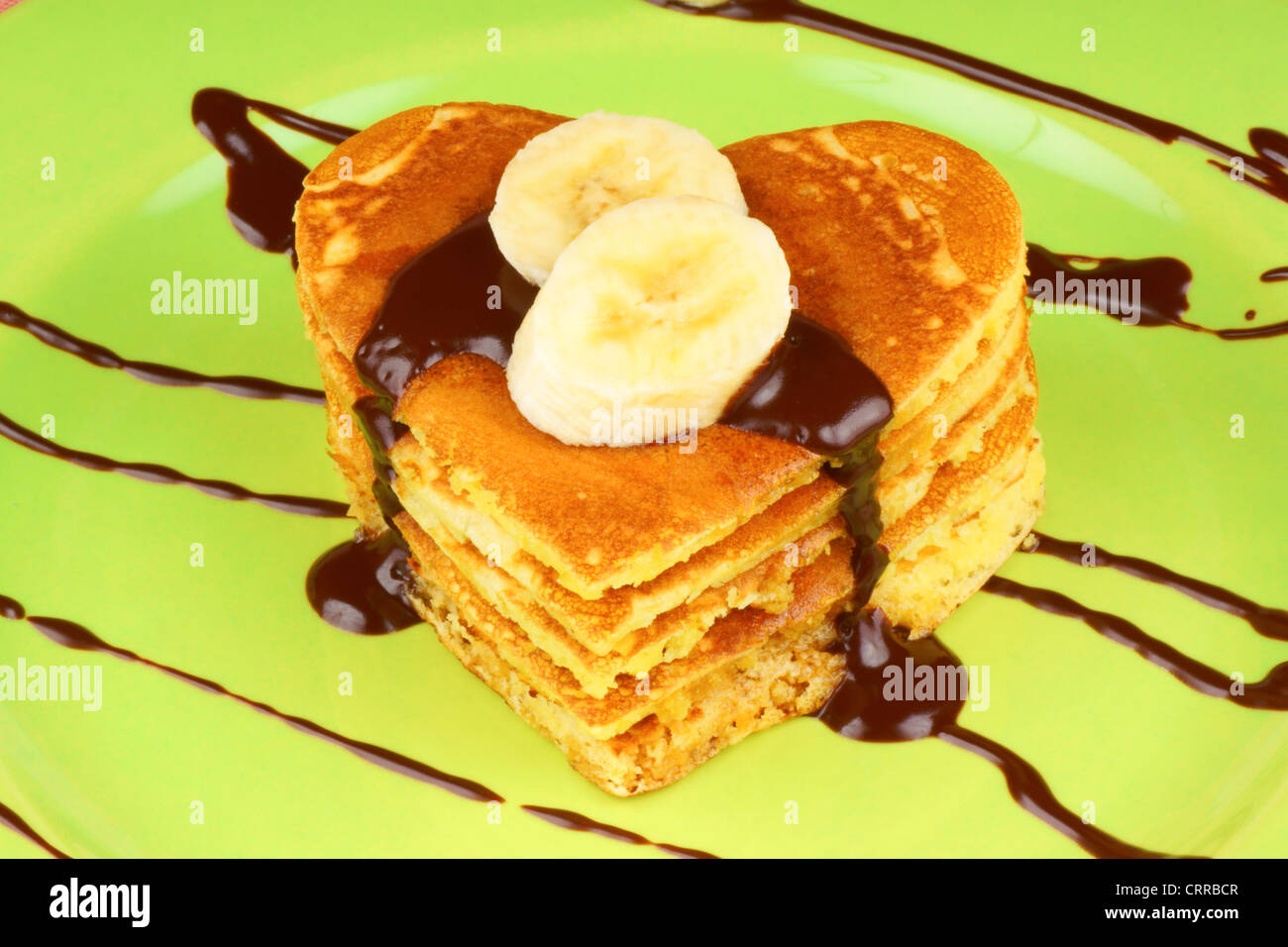 Heart shaped pancakes with chocolate sauce and banana slices on a green dish. A perfect breakfast for Valentine's Day. Stock Photo