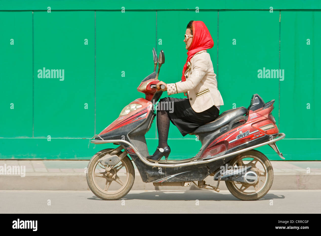 A Chinese woman travels along a road on her scooter in Kashgar. Stock Photo