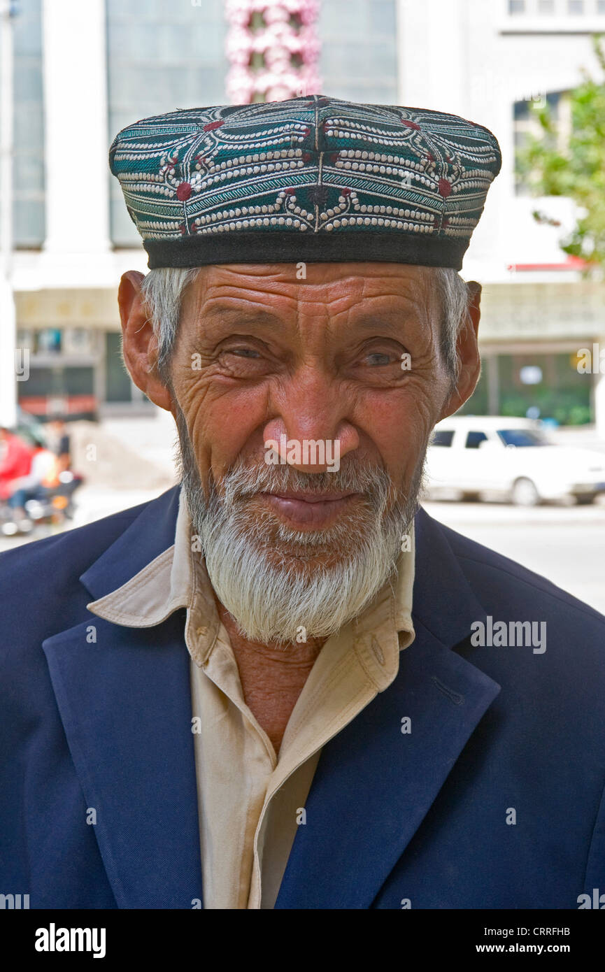 A smiling eldely Uyghur Chinese man poses for the camera in the street in Kashgar wearing the traditional dopa hat. Stock Photo