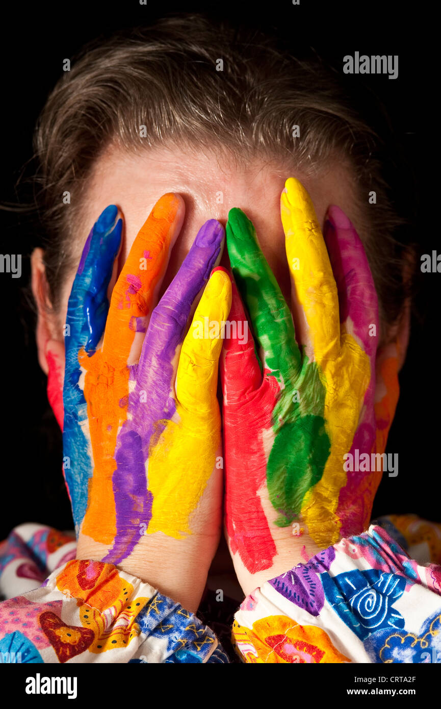 Woman hiding face behind multicolored fingers wearing a colorful clownish top Stock Photo