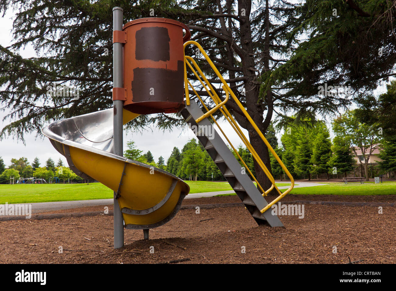 A yellow and red spiral playground slide under a green tree with the