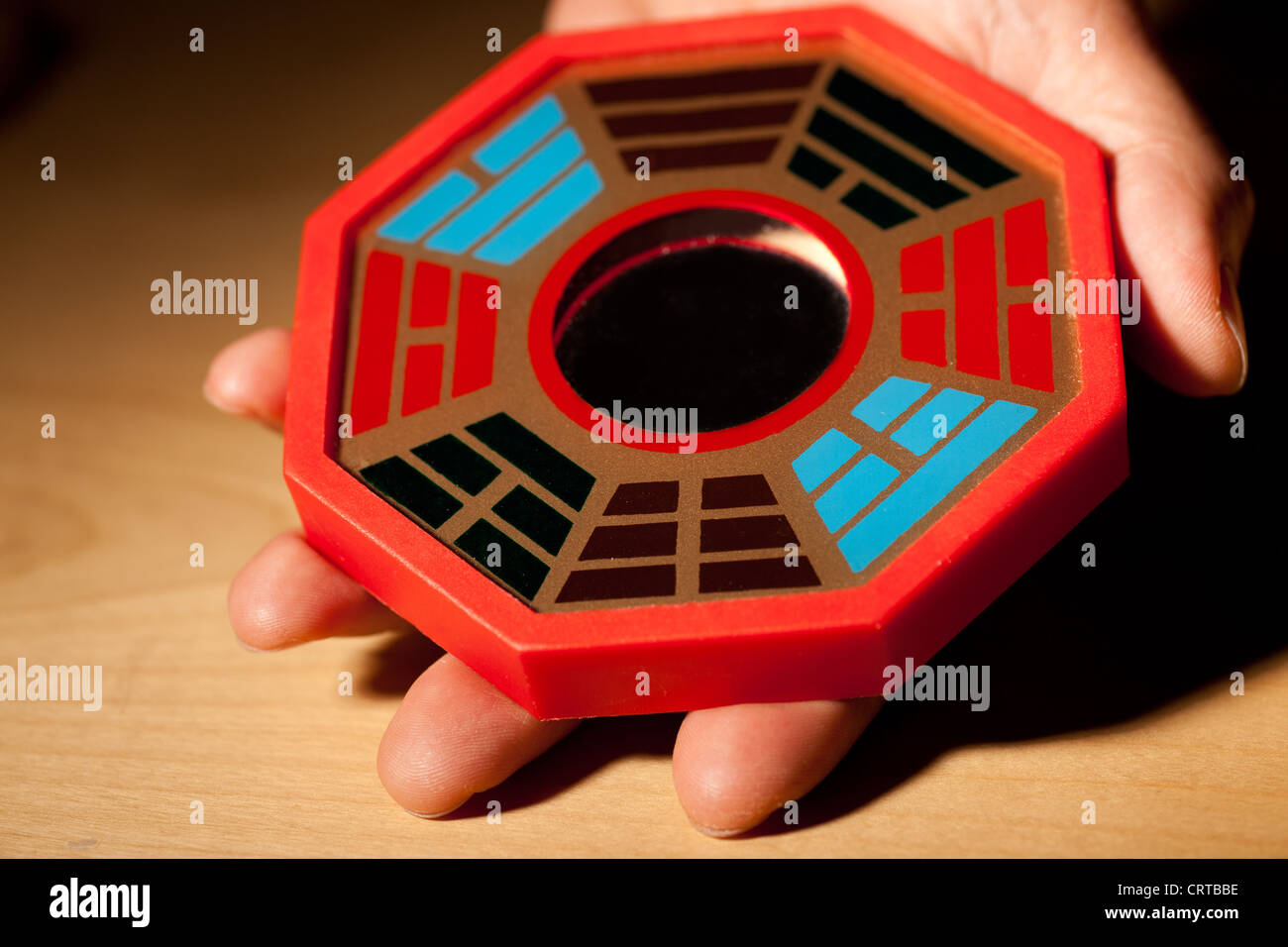 man's hand holding Chinese bagua mirror on wooden table Stock Photo