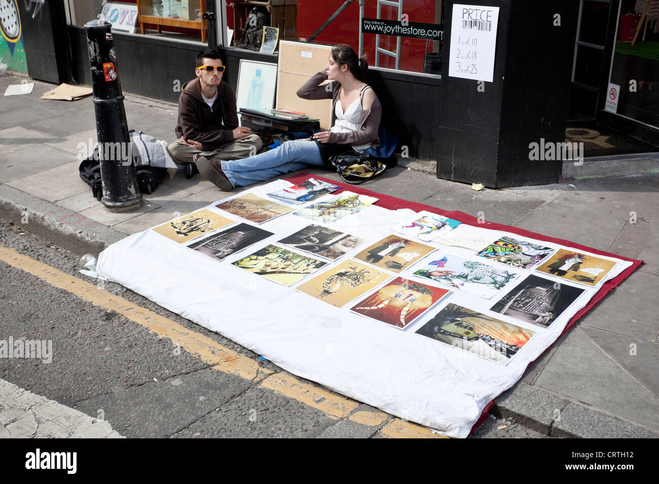 Couple of market traders display paintings for sale on the pavement, Brick Lane, London, England, UK Stock Photo