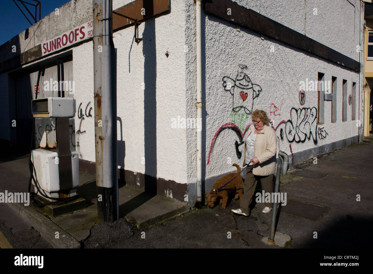 A local woman walks her dog passing a closed garage premises in the City of Galway, Ireland. Stock Photo