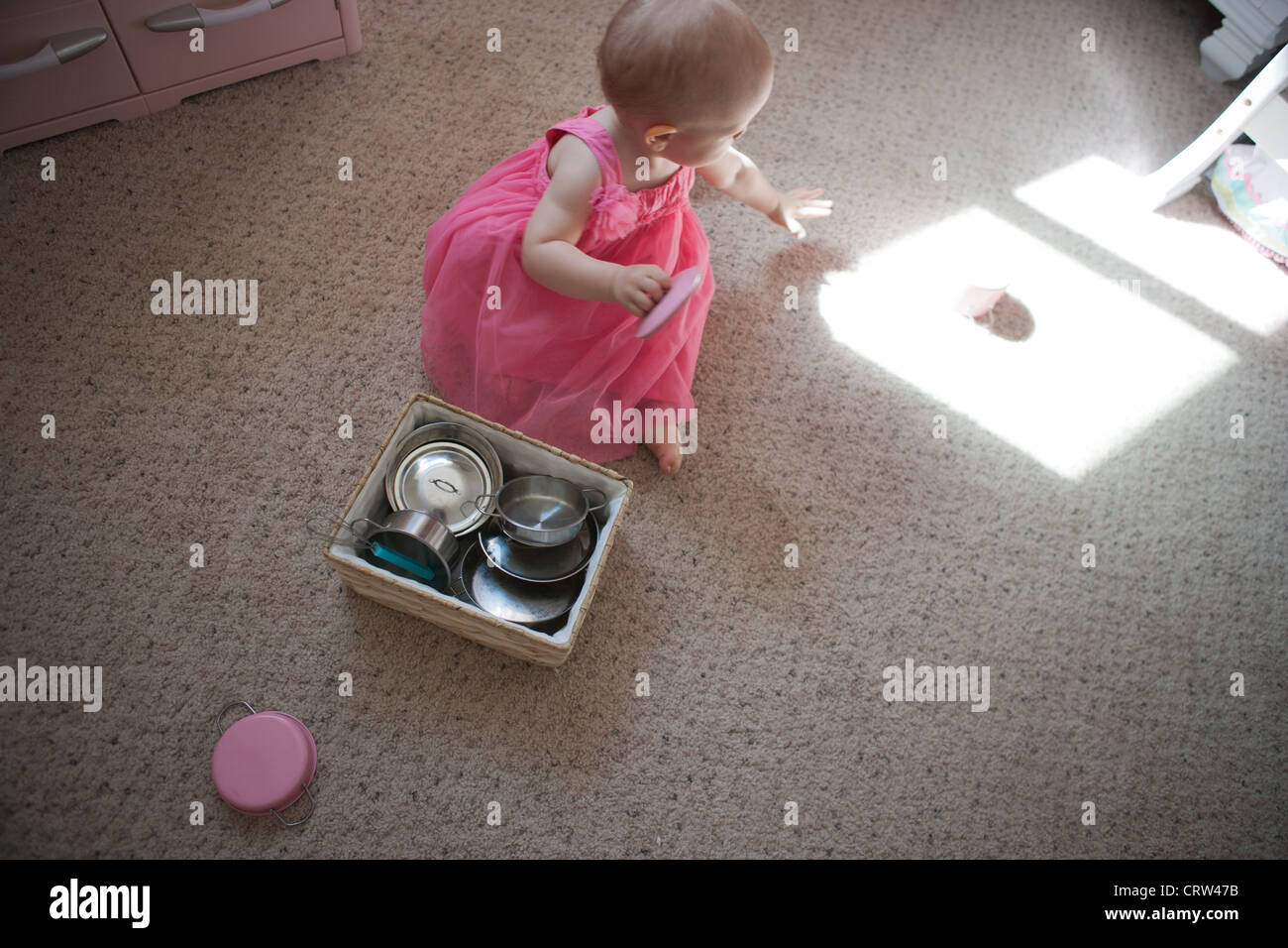 One year old girl plays with toy pots and pans and notices an object in light. Stock Photo