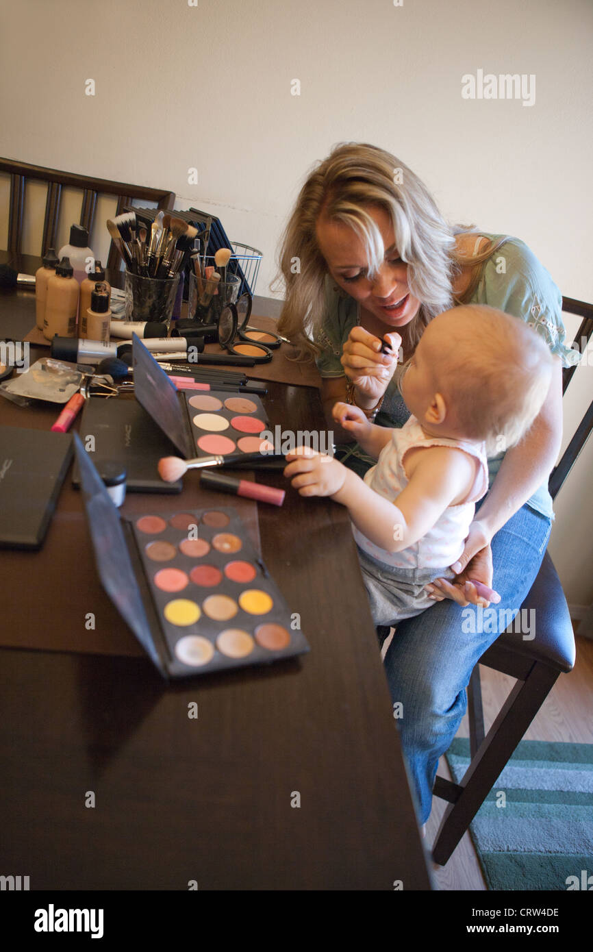 A mom putting makeup on her one year old daughter at home. Stock Photo
