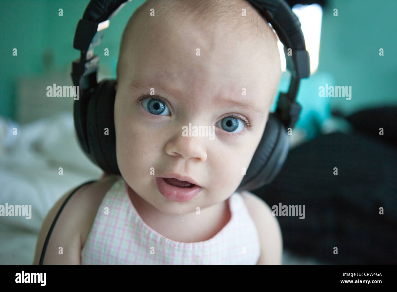 One year old girl wearing large headphones and looking wideeyed Stock