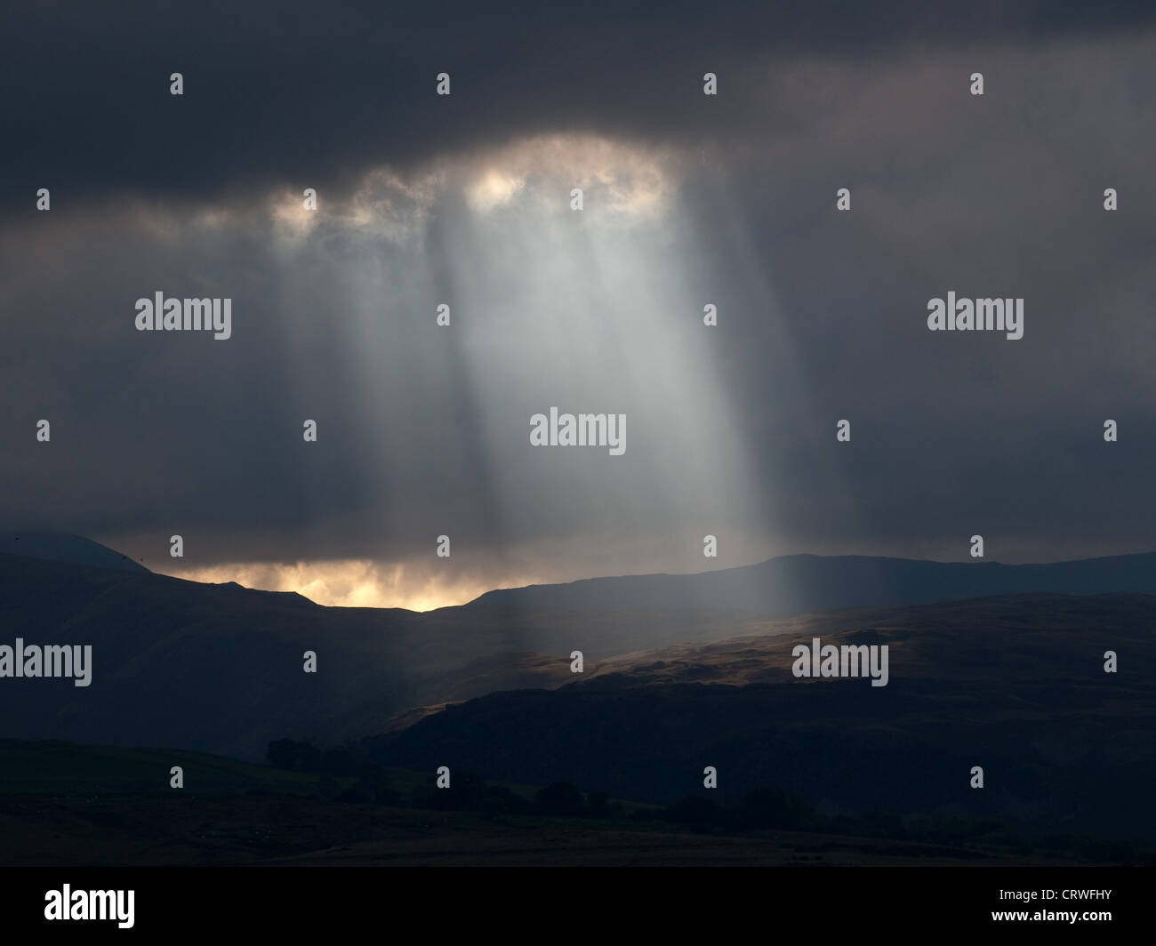 Sunbeams through a dramatic gap in the clouds illuminate Shap fells in Cumbria and the lakeland hills behind Stock Photo