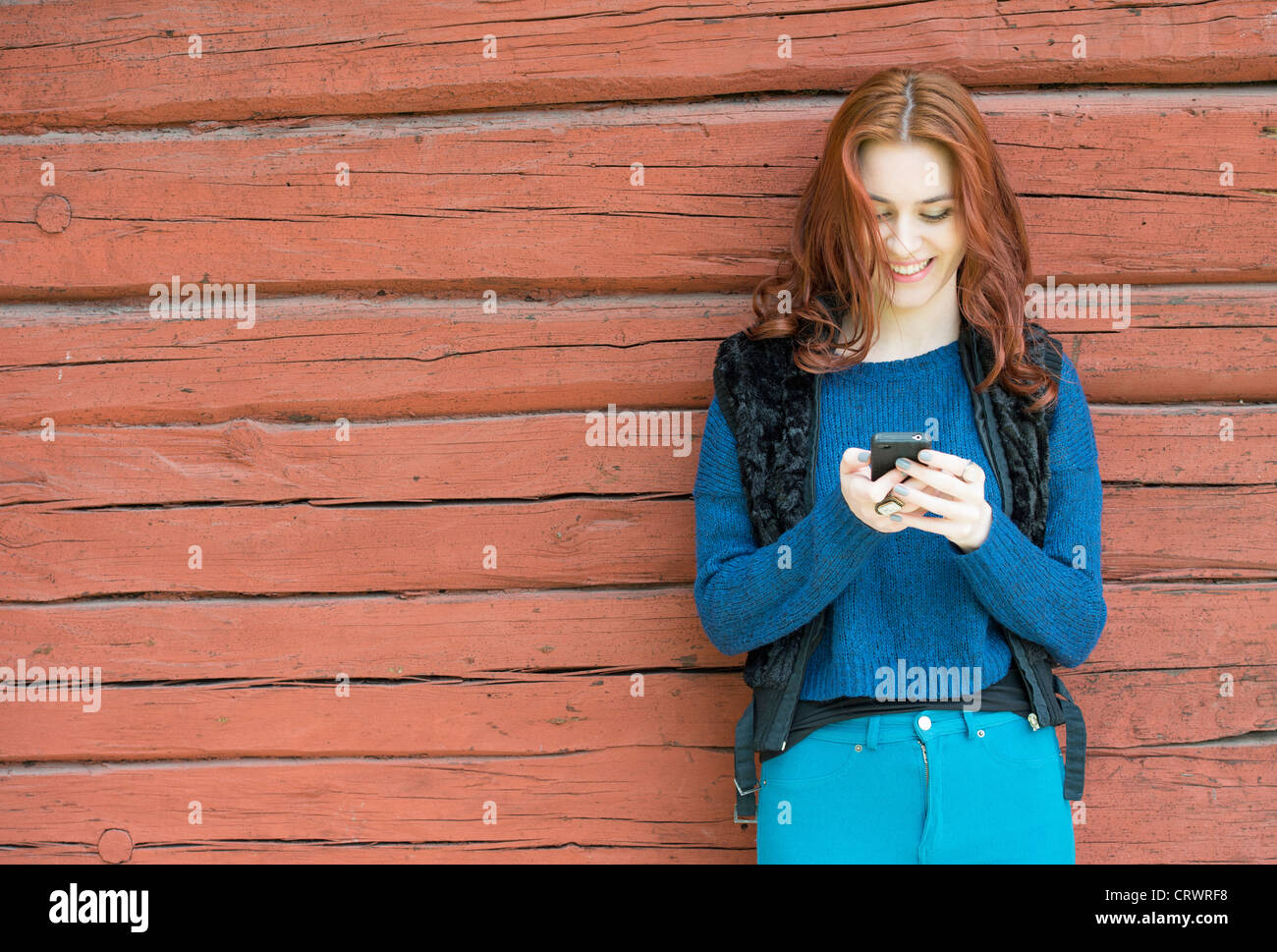 Young woman with red hair laughing and reading a text message on her phone Stock Photo