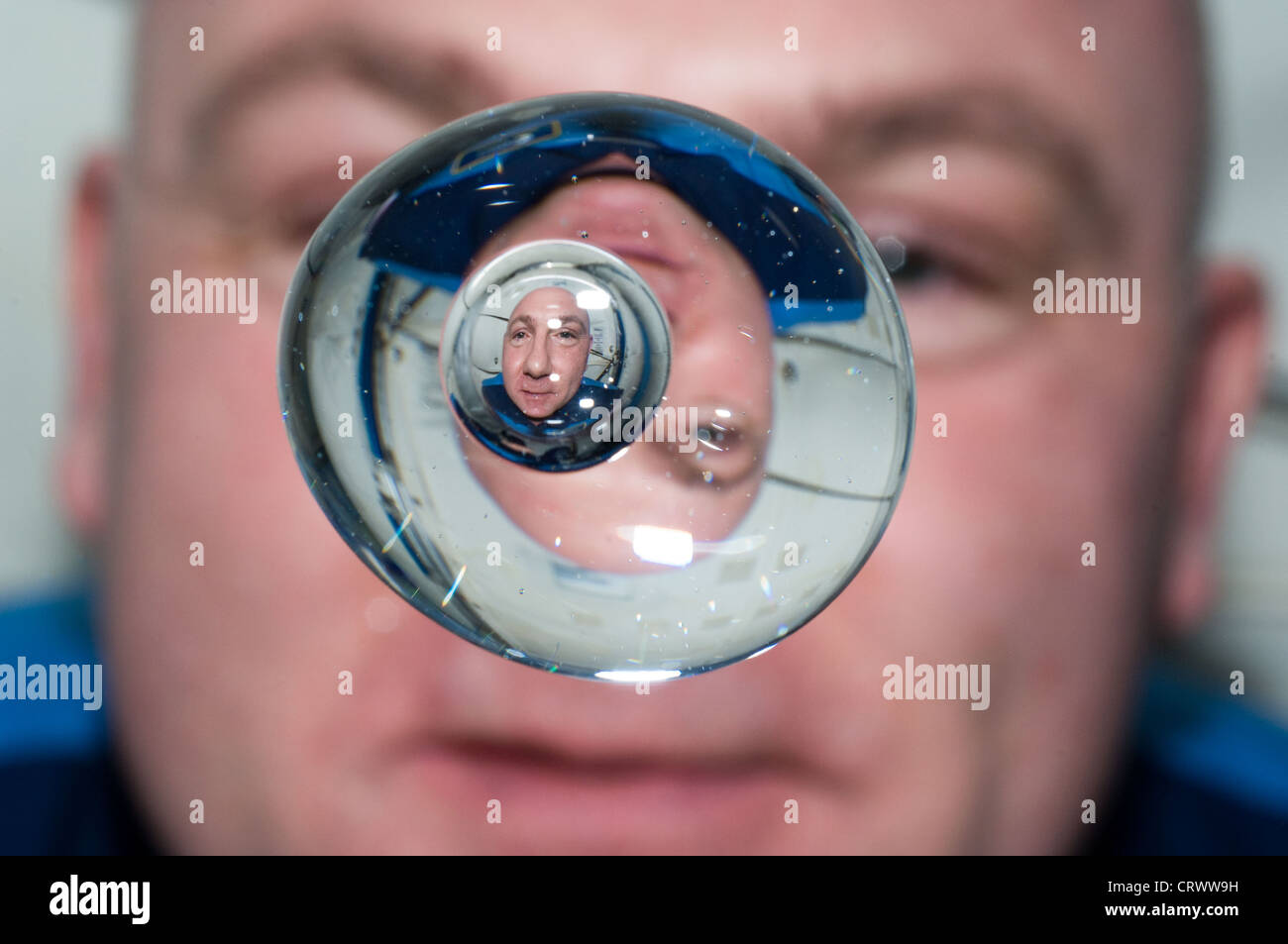European Space Agency astronaut Andre Kuipers watches a water bubble showing his reflected image float freely in zero gravity aboard the International Space Station June 24, 2012. Stock Photo